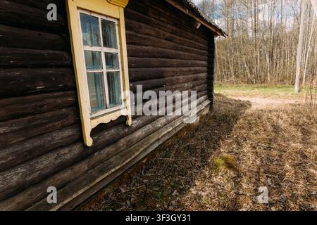 Log wall of an old abandoned house with a yellow window Stock Photo