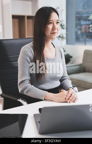 young woman is working on laptop in modern office environment, showcasing focused and productive atmosphere. She is dressed in professional white shir Stock Photo