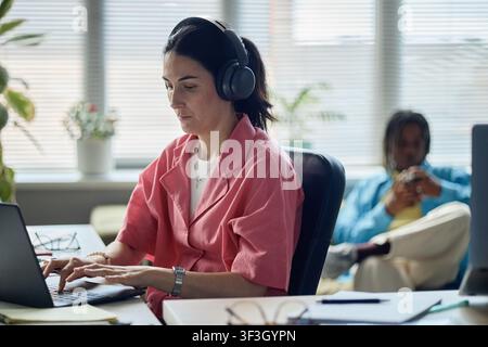 Adult Woman Working on Laptop with Headphones in Office Stock Photo