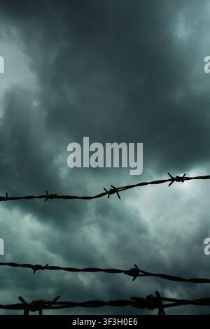 Silhouetted strands of barbed wire against dark turbulent storm clouds, evoking confinement, danger, conflict and restricted freedom Stock Photo