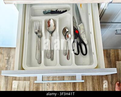 Cutlery and kitchen tools are organized in a drawer during a typical day at home. The setting includes various utensils and a pair of scissors. Stock Photo