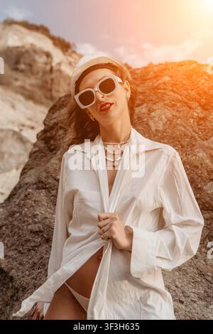 Woman sunglasses helmet stylish woman in safety gear and white shirt poses against a rocky cliff with copy space Stock Photo
