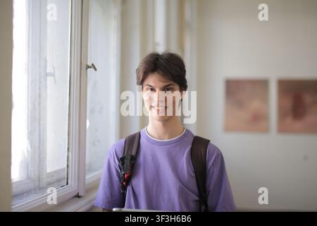 Young male student with a backpack smiling by a window Stock Photo