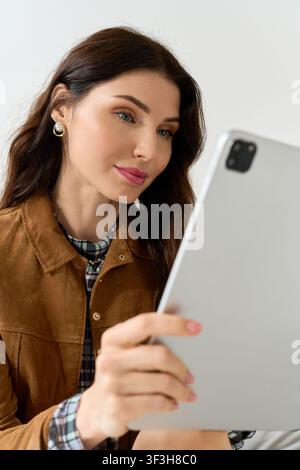 This beautiful young woman dressed in sophisticated attire engages with her tablet, exuding style. Stock Photo