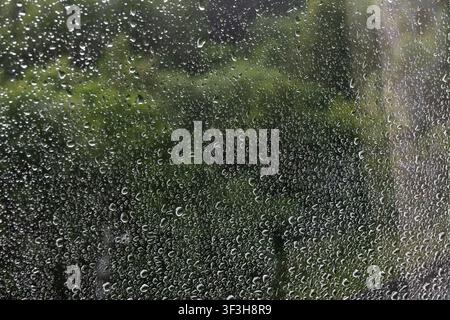 Horizontal close-up of raindrops on a window pane against a dark green blurred background. Great for abstract water textures, moody backgrounds, and r Stock Photo