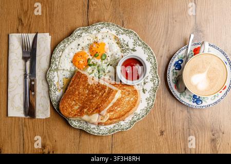 Fried egg breakfast with toast on a vintage plate. Isolated on a wooden table. Coffee and cutlery. Stock Photo