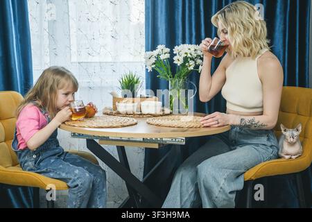 Mother and daughter having tea together at home with a pet cat Stock Photo
