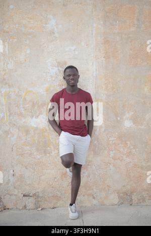 Confident young Black man leaning against a weathered wall Stock Photo