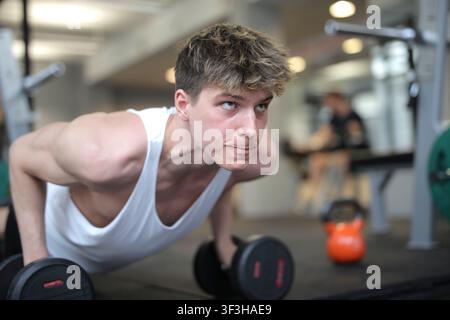 Fit young man doing dumbbell push ups in gym Stock Photo