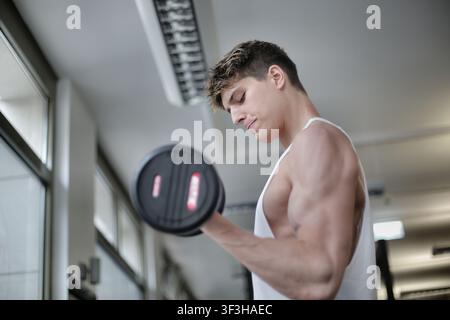 Young muscular man doing bicep curls with dumbbell Stock Photo