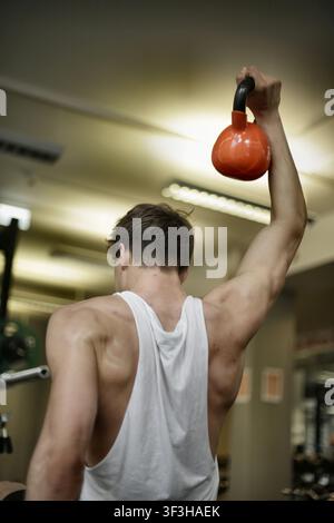 Back view of fit man lifting a kettlebell overhead Stock Photo