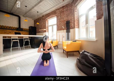 Woman meditating on yoga mat by joining hands behind back Stock Photo