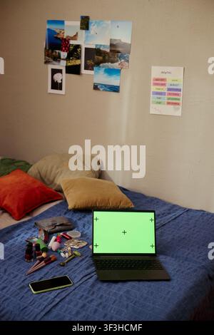 Vertical shot of laptop displaying green screen on bed beside smartphone and cosmetics, suggesting influencer content planning or remote shopping. Ideal for digital lifestyle ads Stock Photo