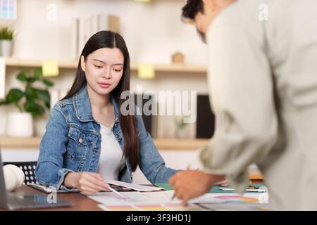 Asian fashion designers collaborating on sketches in creative studio Stock Photo