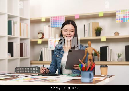 Asian female graphic designer working on digital tablet at creative studio desk Stock Photo