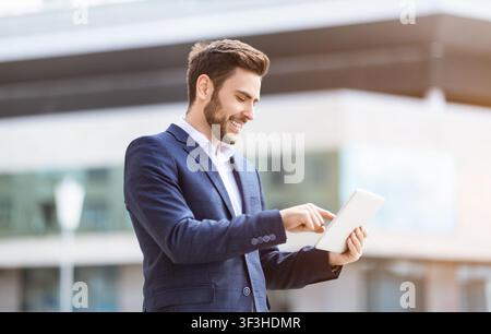 Handsome young office worker with tablet computer browsing web on city street Stock Photo
