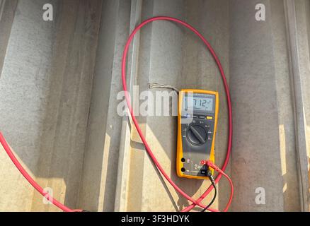 Close-up of a digital multimeter measuring DC voltage output from a photovoltaic solar panel during system testing and inspection. Electrical testing Stock Photo