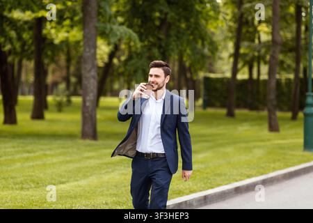 Smiling entrepreneur drinking his morning coffee from paper cup during walk in park Stock Photo