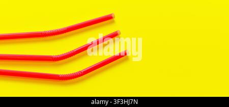 Three pink plastic drinking straws on yellow board, view from above Stock Photo