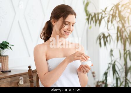 Smiling lady wrapped in towel using body or face cream Stock Photo