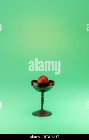 Conceptual studio food photograph of a single brown egg displayed on a dark glass pedestal stand against a mint green gradient background. The minimal Stock Photo