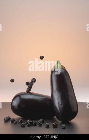 A vertical conceptual food art image featuring dark purple eggplants and several black berries floating in mid-air against a neutral gradient backgrou Stock Photo