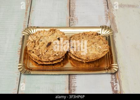 Two almond florentine cookies on a shiny gold tray over a distressed wooden background. Stock Photo