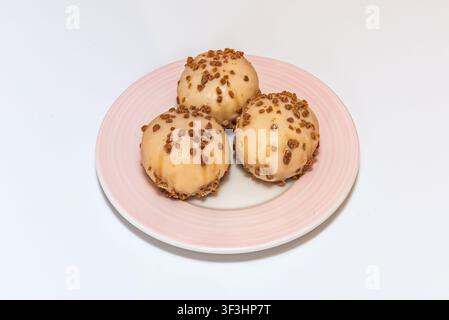 Three round dessert balls covered in beige glaze and sprinkled with crunchy bits on a pink plate. Stock Photo