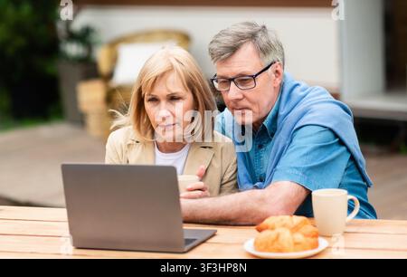 Serious mature couple using laptop computer near camper van outside Stock Photo