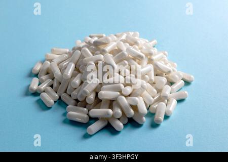 A large pile of white capsules lies on a cerulean blue background. The capsules are glossy, cylindrical, and uniformly shaped, reflecting light to cre Stock Photo