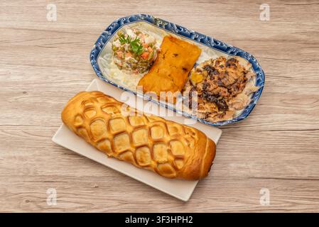 Braided Stuffed Bread Loaf Beside Blue-Patterned Platter with Salad, Tamale, and Grilled Meat Stock Photo