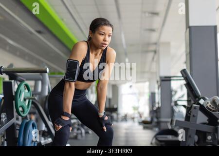 Exhausted young Black woman catching her breath after intense workout in gym Stock Photo