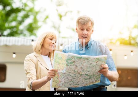 Mature husband and his wife reading map near camper van in countryside Stock Photo