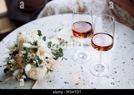 Elegant bridal bouquet beside two champagne flutes filled with amber beverage on a speckled table surface. Romantic wedding toast celebration Stock Photo