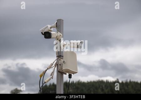 Multiple modern surveillance cameras mounted on a pole with exposed wiring, actively monitoring an outdoor area under a cloudy sky, representing conce Stock Photo