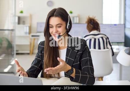 Female call center agent with headset on laptop video chat in modern office Stock Photo