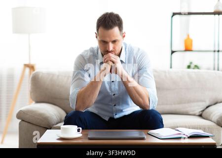 Pensive young guy sitting at table, looking at table Stock Photo