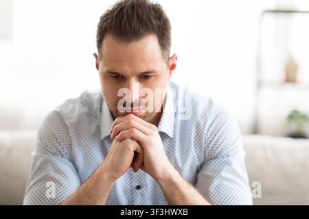 Pensive young guy sitting on couch, looking down Stock Photo