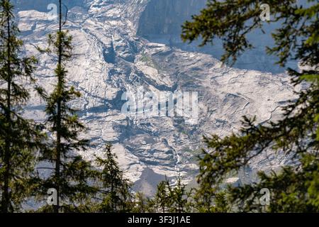 Kandersteg, Switzerland - June 25, 2026: Bright daylight illuminates the rugged gray rock face of a massive alpine mountain wall framed naturally by e Stock Photo