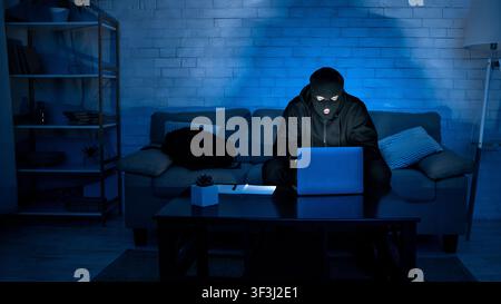 Masked criminal downloading private information using pc Stock Photo