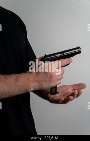 Cropped profile shot of man hands inserting loaded metal magazine into semi automatic pistol handle against neutral studio background. Stock Photo