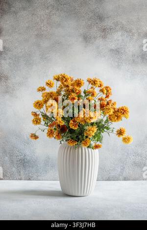 Autumn bouquet of yellow and orange chrysanthemums arranged in white ceramic vase against neutral textured background. Minimal seasonal floral composi Stock Photo