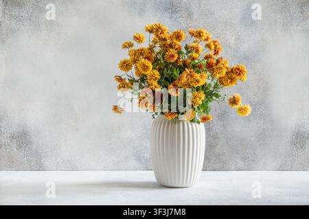 Autumn chrysanthemum bouquet of yellow and orange flowers in white ceramic vase on neutral gray background. Minimal autumn floral still life for home Stock Photo