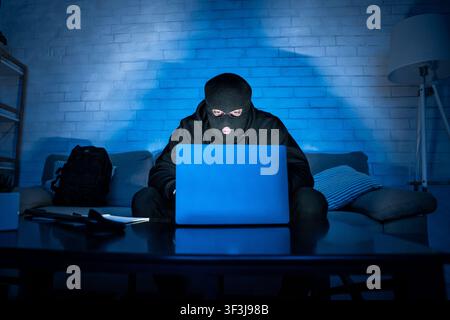 Masked hacker downloading private information using pc Stock Photo