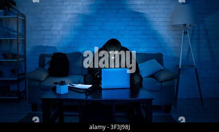 Masked hacker downloading private information using laptop Stock Photo