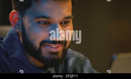 Close up Indian smiling business man looking in digital tablet at night office Arabian businessman amazed with good financial result Hindu male guy Stock Photo