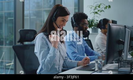 Happy Caucasian business woman working in call center talking winning celebrating good news successful trading near multiethnic operators team Stock Photo