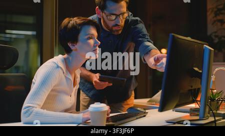 Business team employers with computer discuss work at night evening office Caucasian man leader checking working process help with difficult task Stock Photo