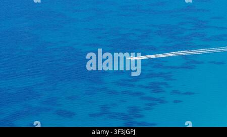 Possidi beach, Greece 11 July 2026. A small motorboat creates white trails as it speeds through the clear deep blue waters of Possidi beach in Greece Stock Photo