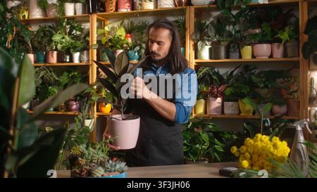 Portrait of beautiful professional caucasian male florist holding plant looking at camera. Confident young adult man working at florist shop taking Stock Photo